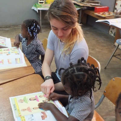 A Projects Abroad volunteer helps with homework during her childcare volunteering in Jamaica for groups. A volunteer works with children on English lessons in Jamaica with a group.